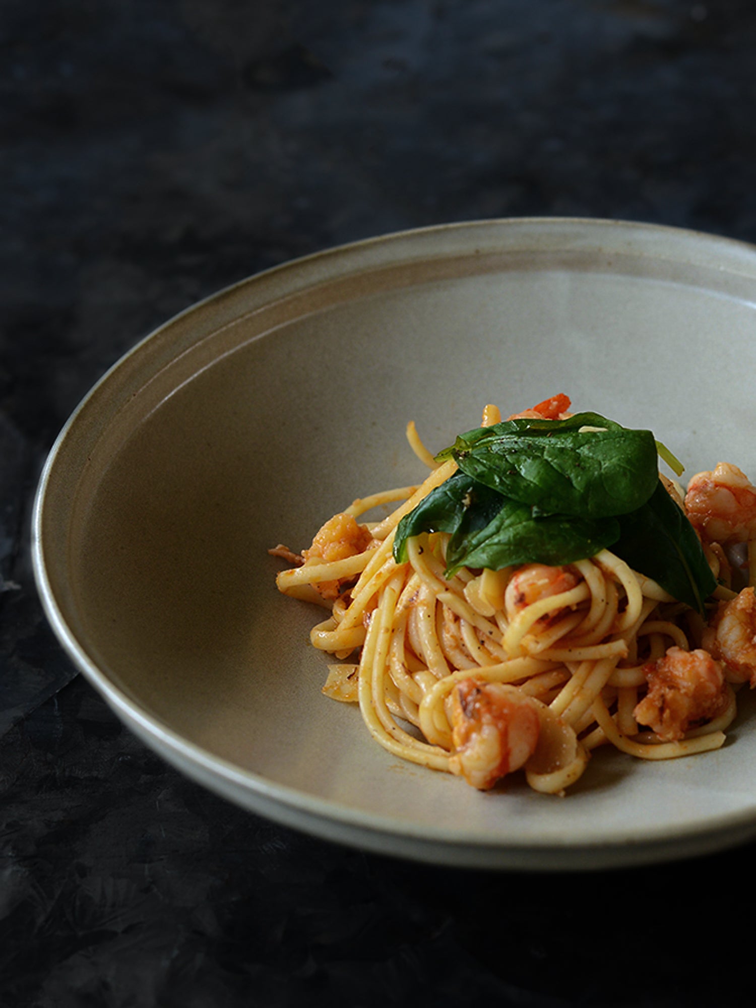Spaghetti dish with shrimp and spinach on a dark background